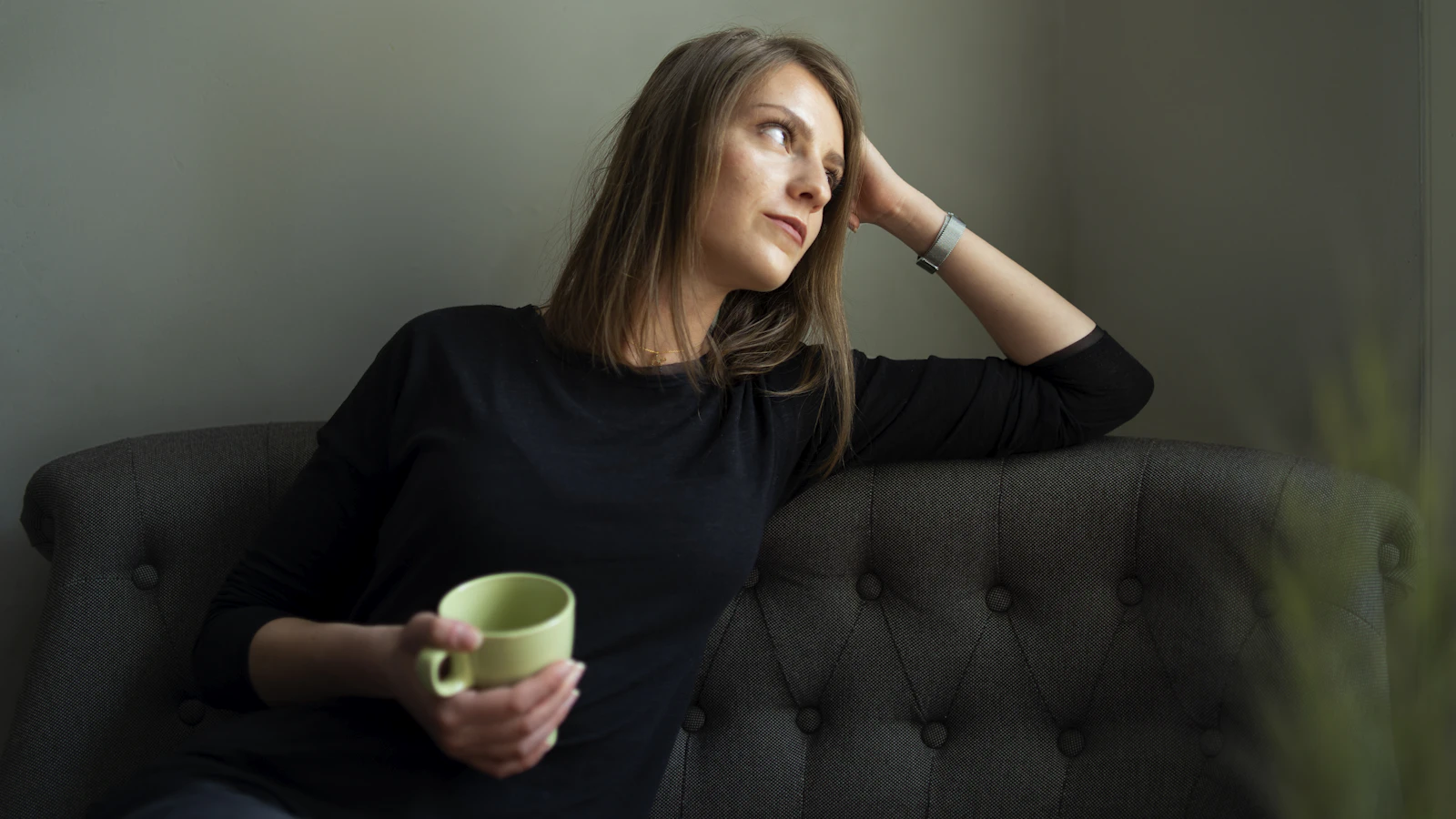Vrouw rust uit op een bank met een kop thee bij daglicht.