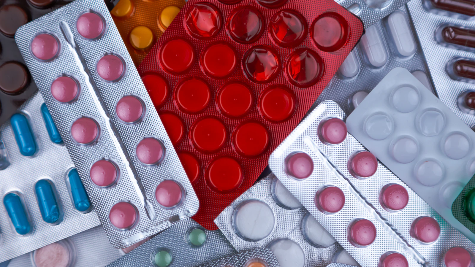 Een stapel doordrukstrips met tabletten en capsules in verschillende kleuren, van bovenaf gefotografeerd.
