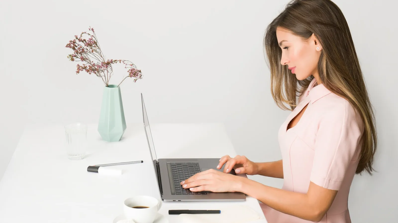 Een vrouw werkt aan een laptop aan een lichte tafel.