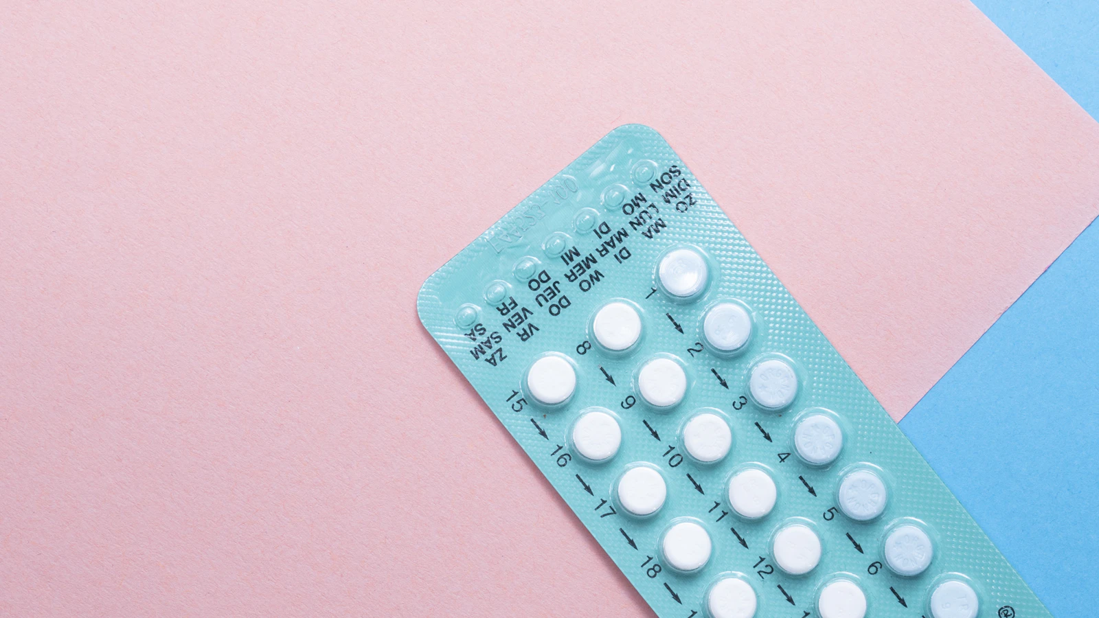 Muntgroene anticonceptiestrip met genummerde tabletten en dagaanduidingen op een roze ondergrond.