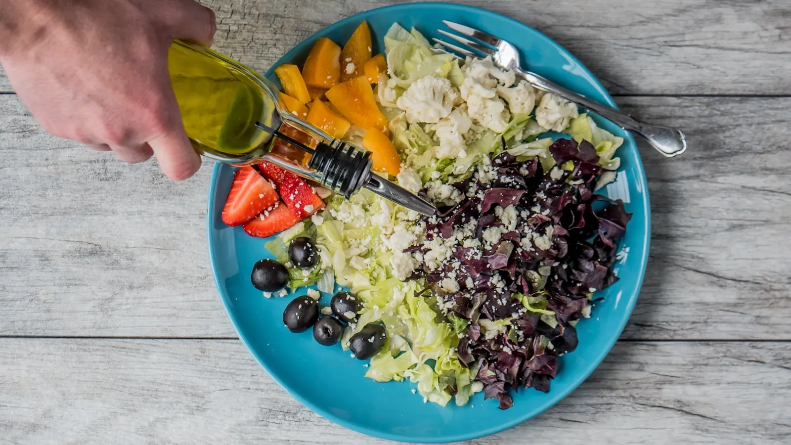 Olijfolie wordt over een kleurrijke salade met sla, mango en aardbeien geschonken.