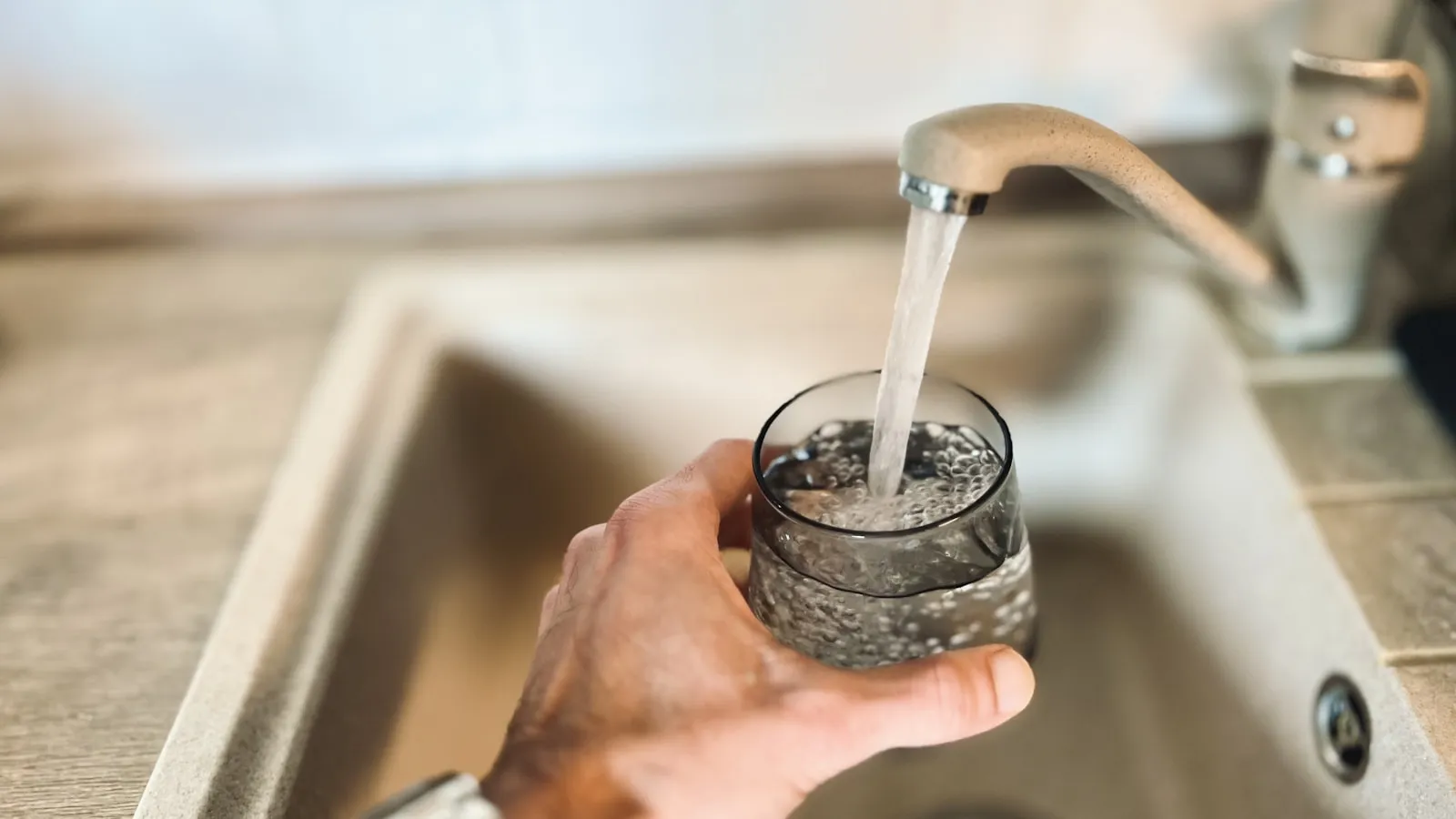 Hand houdt een glas onder de kraan en vult het met water.
