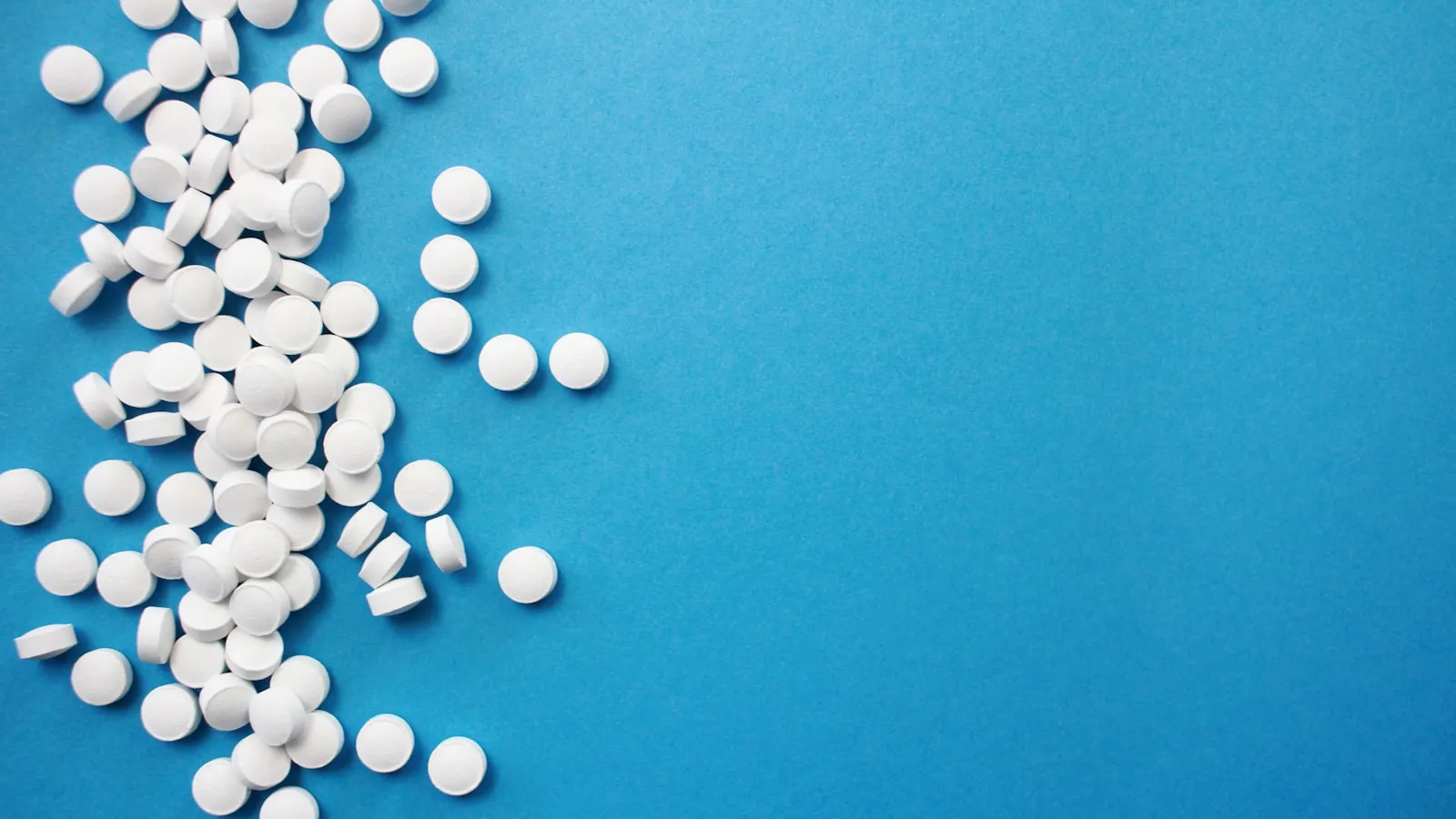 Ronde witte tabletten verspreid op een blauwe ondergrond.