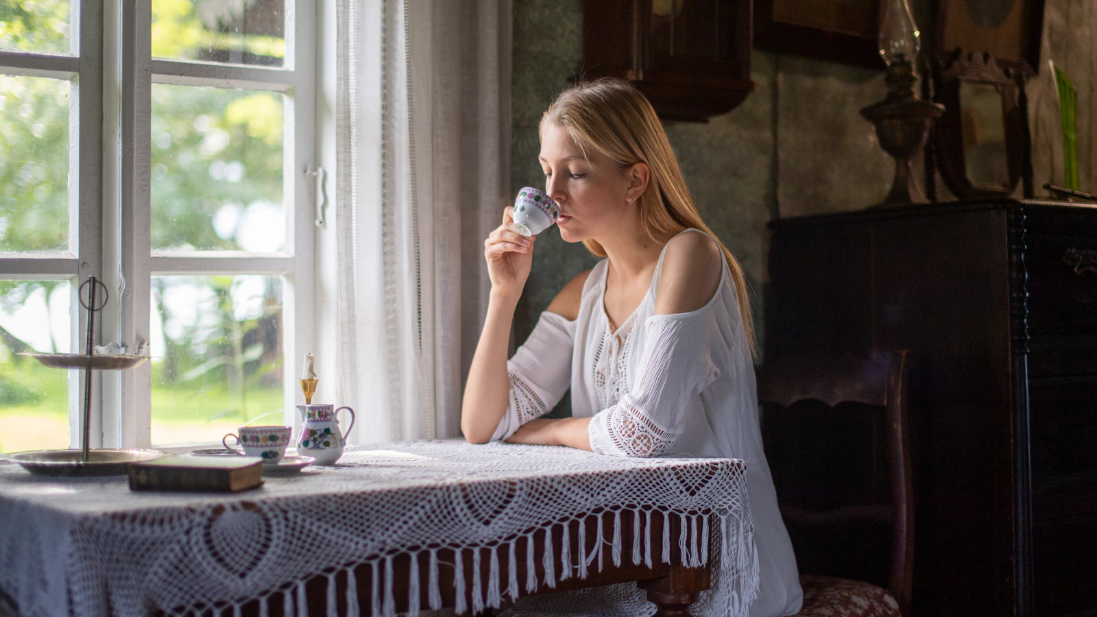Jonge vrouw drinkt rustig thee bij het raam in het ochtendlicht.