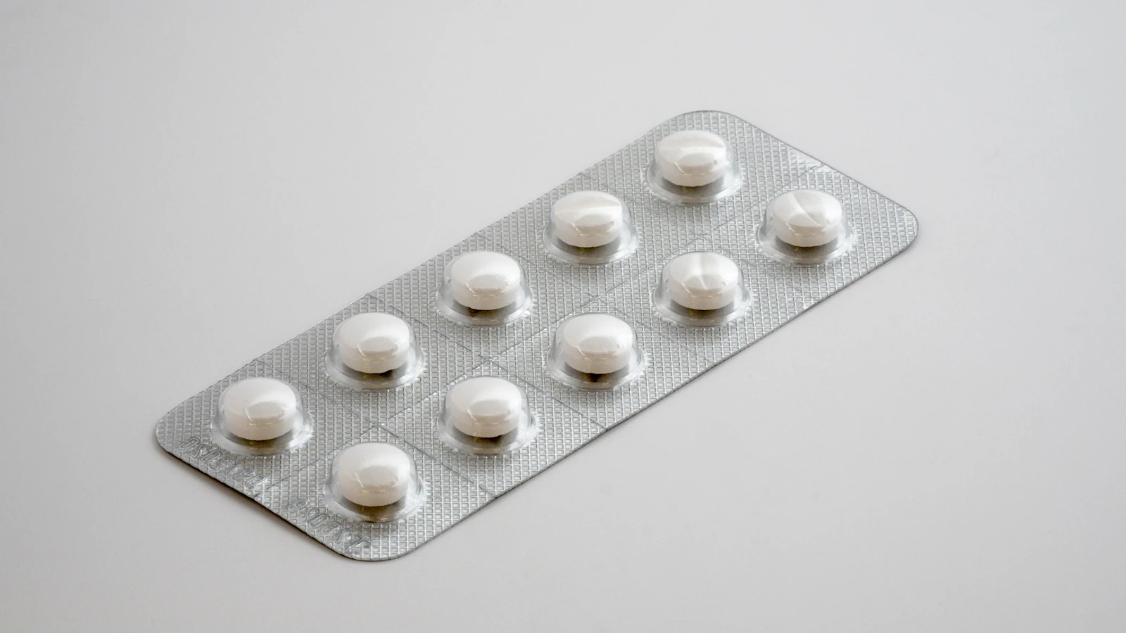 Eén zilverkleurige doordrukstrip met witte tabletten op een lichtgrijze ondergrond.