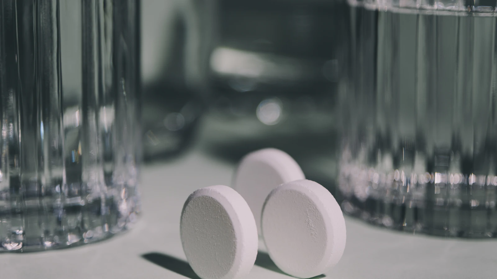 Twee witte tabletten op tafel tussen twee glazen water.