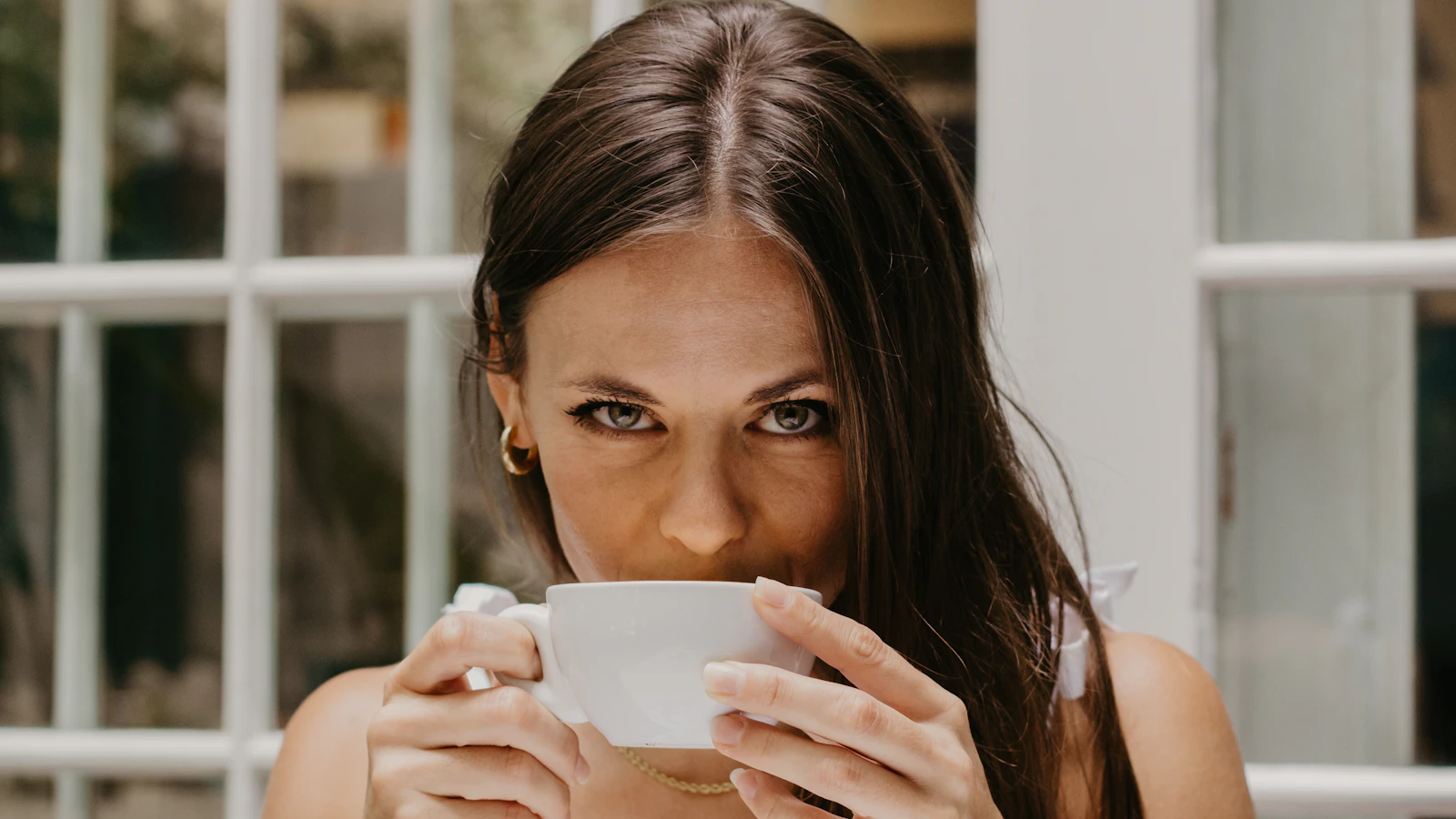Vrouw drinkt rustig uit een kopje bij het raam in de ochtend.