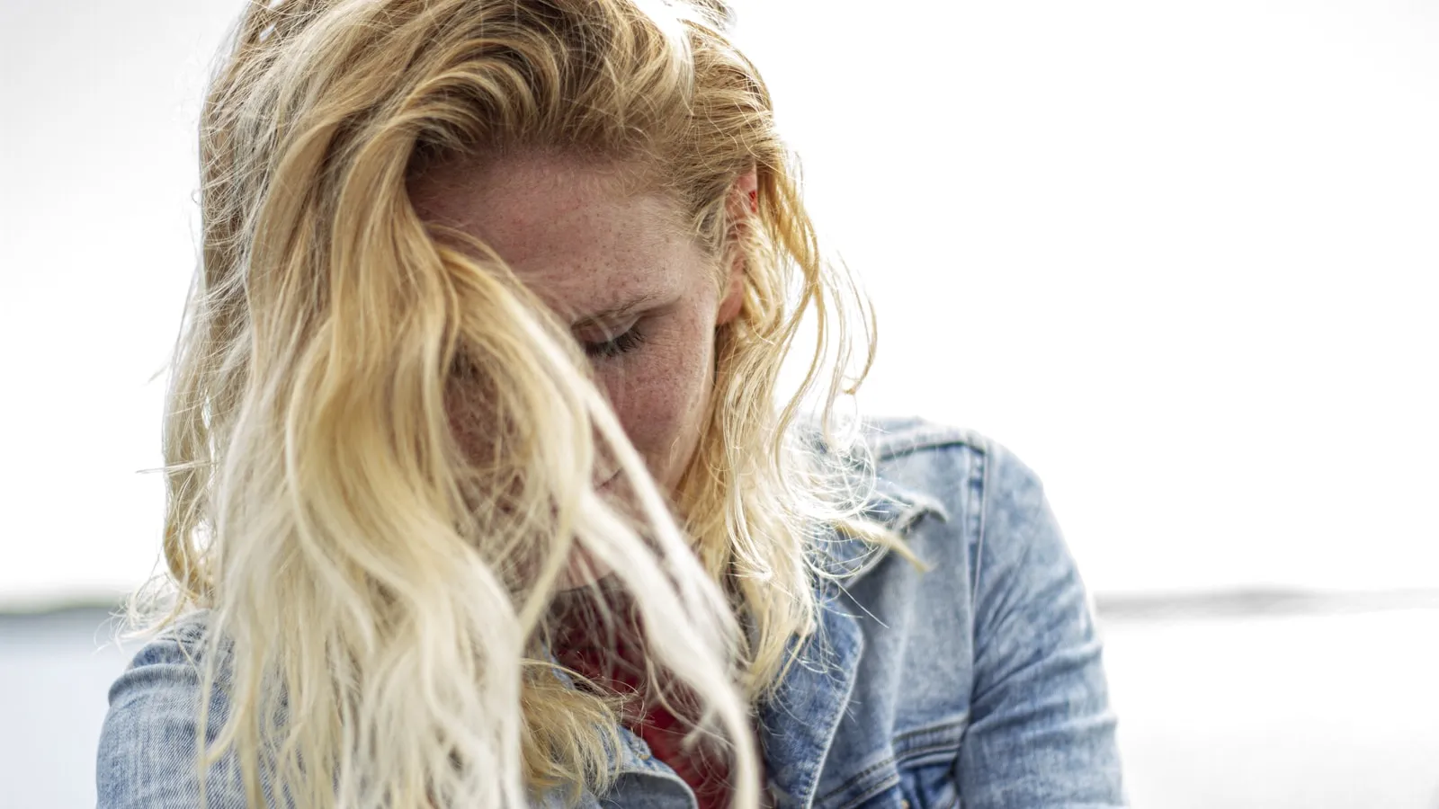 Vrouw met blond haar kijkt omlaag, buiten bij daglicht.