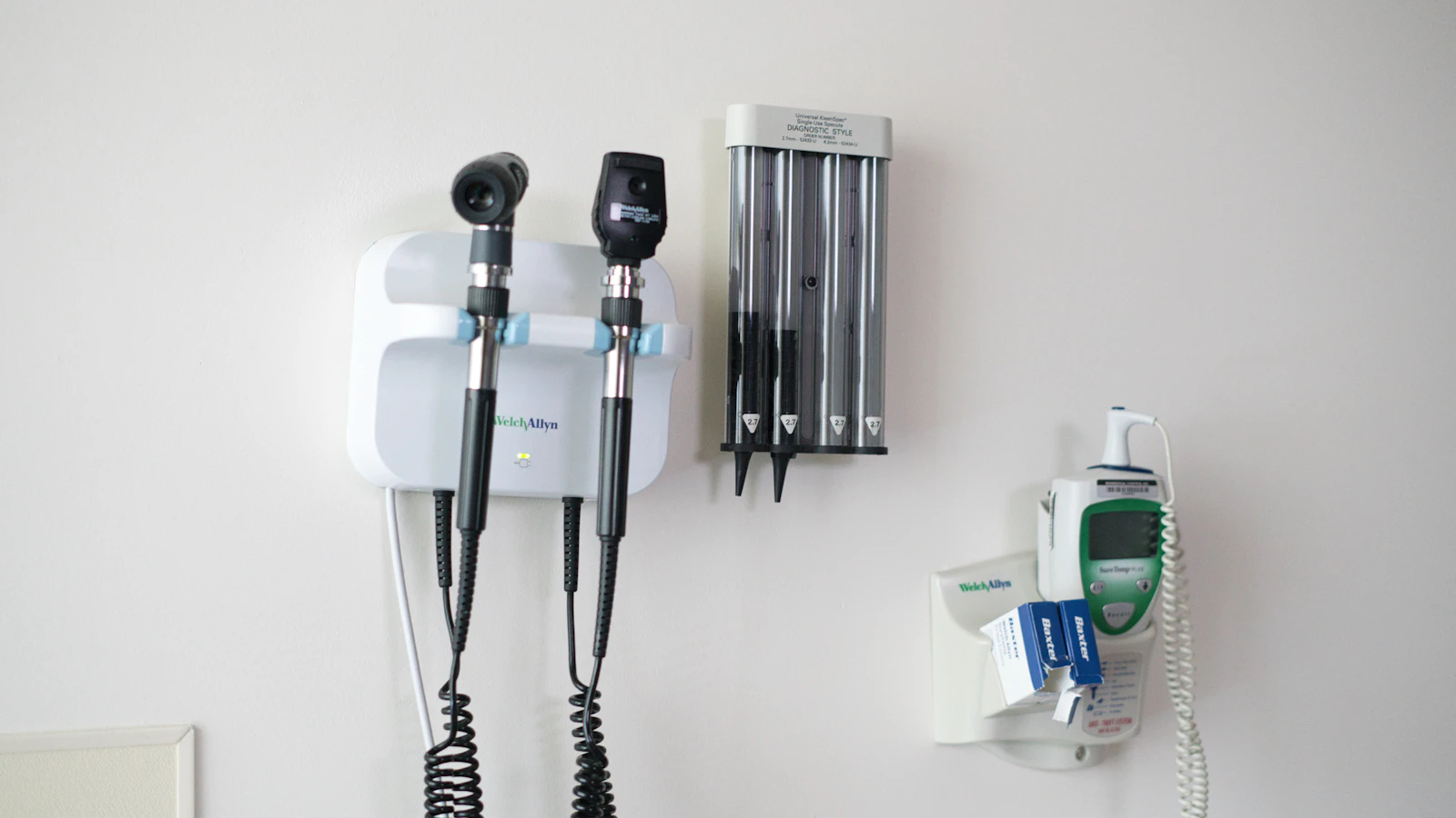 Onderzoeksinstrumenten aan de muur van een spreekkamer, met een otoscoop, oogspiegel en thermometer.