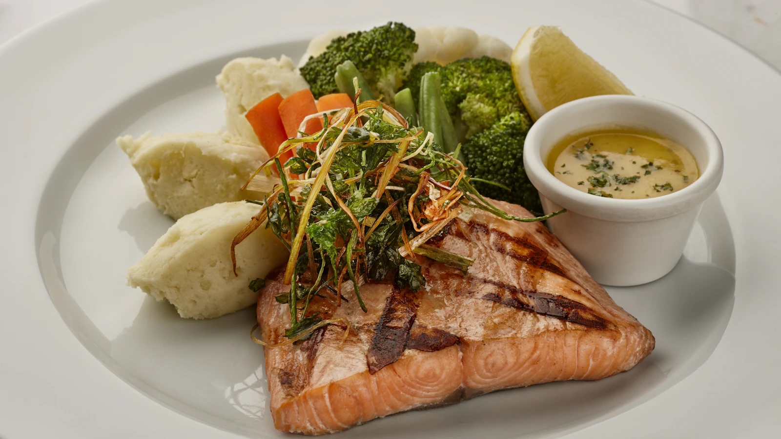 Bord met gegrilde zalm, groente en aardappel op een lichte tafel.