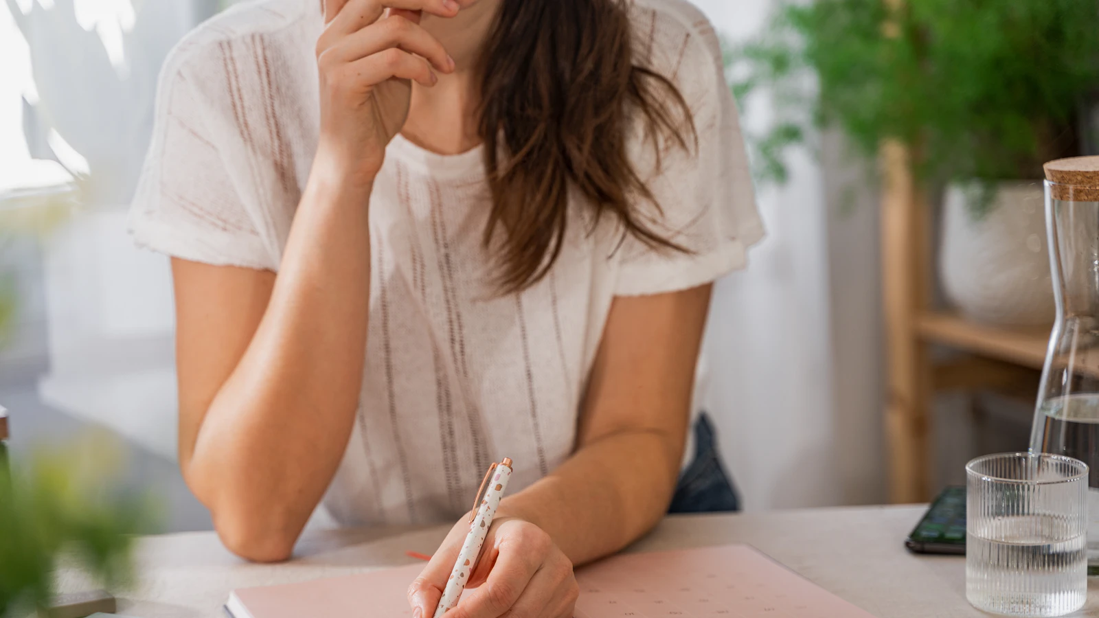A woman writes something on a sheet of paper at a table.