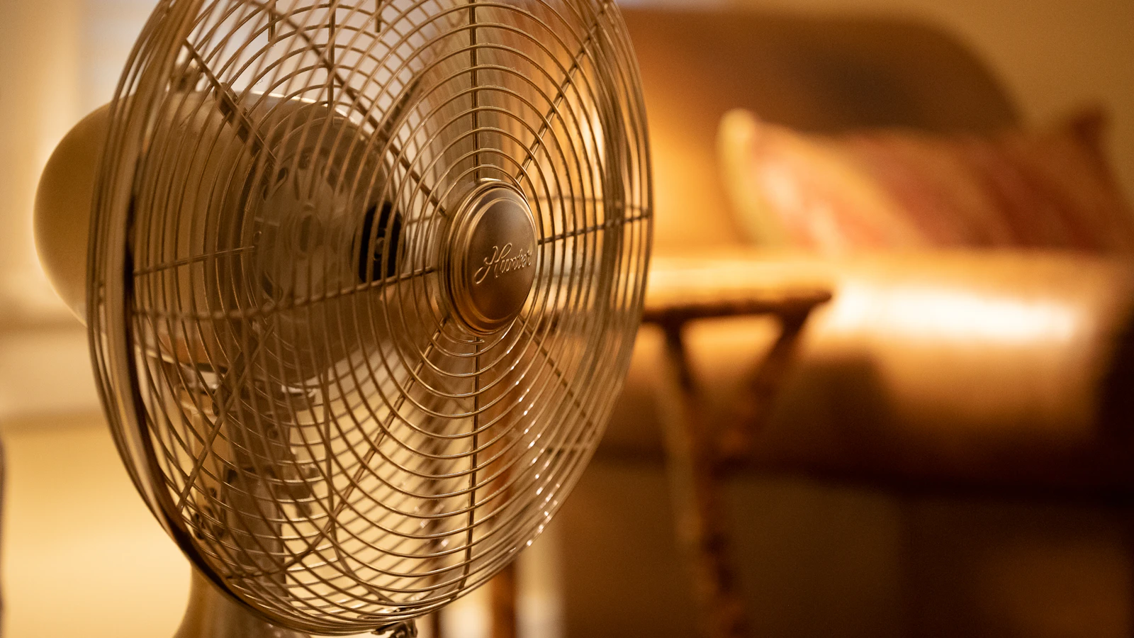 Witte staande ventilator staat aan in een warm verlichte woonkamer.
