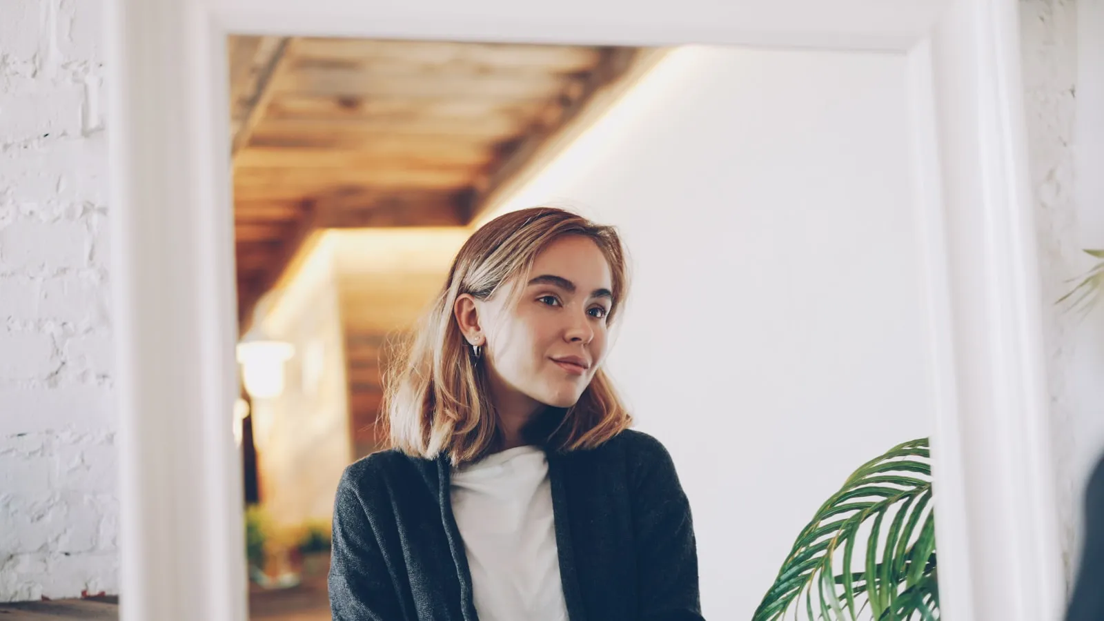 Een vrouw ziet zichzelf weerspiegeld in een spiegel in een lichte kamer.