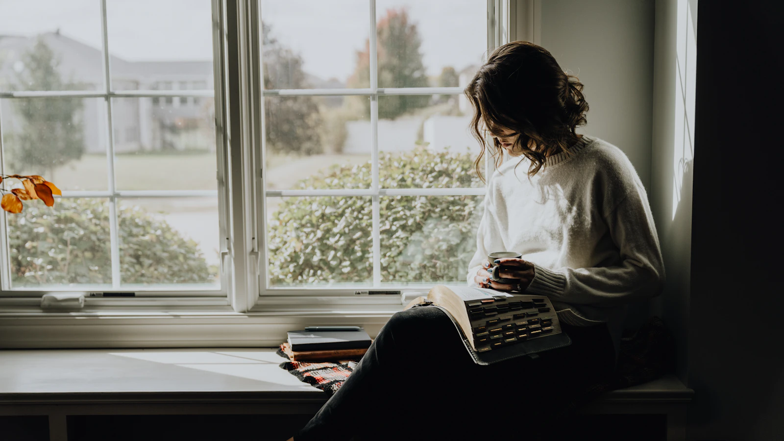 Vrouw leest een boek met een mok in haar handen.