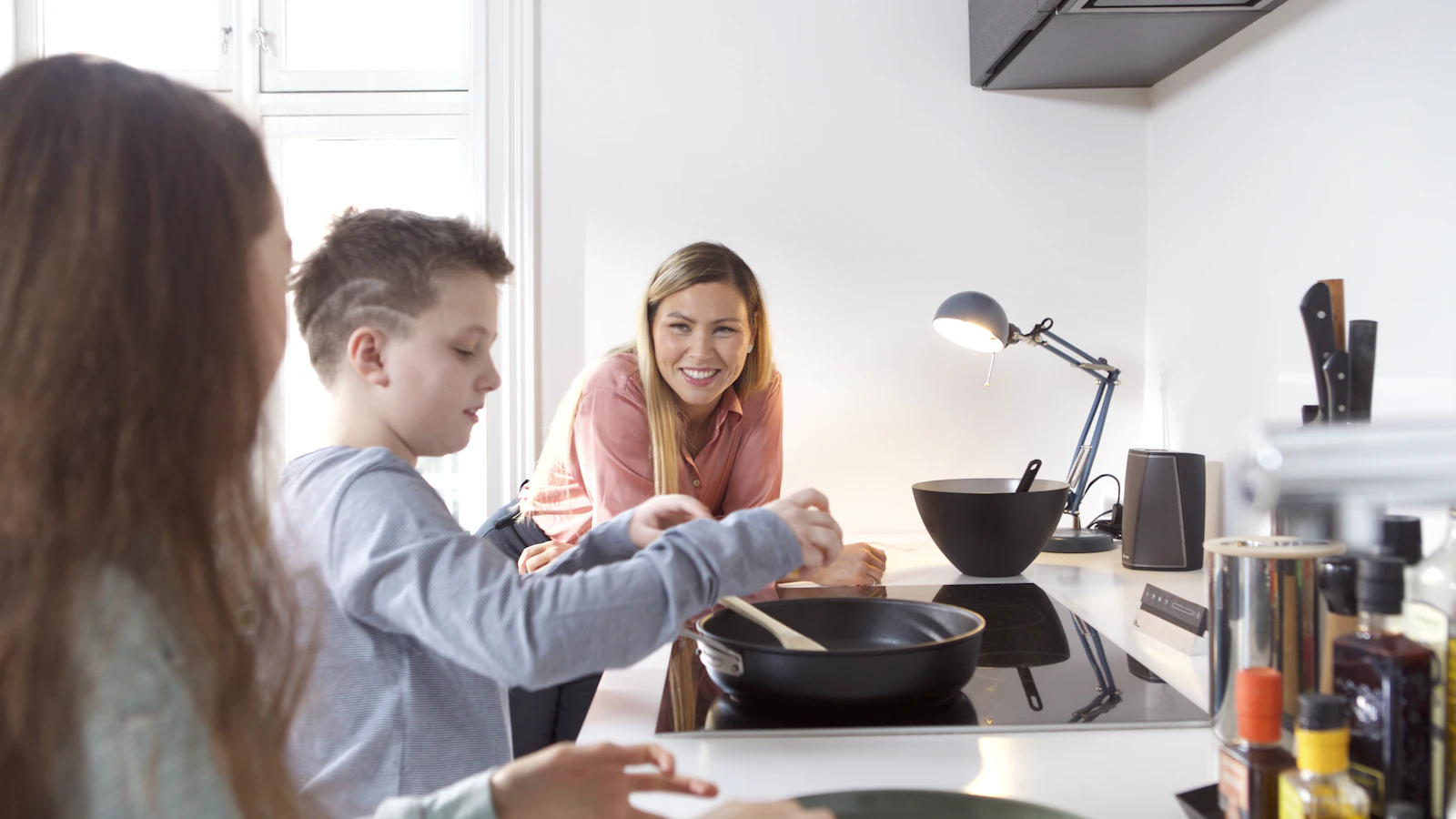 Moeder kookt samen met twee kinderen in een lichte keuken.