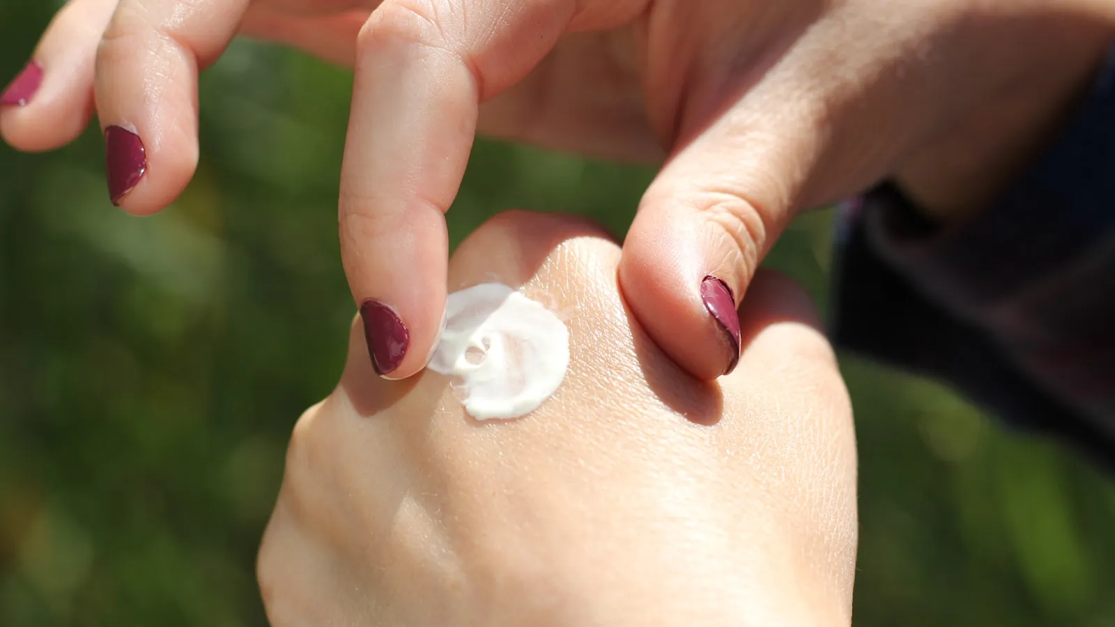 Vrouw brengt een klodder crème aan op de rug van haar hand.