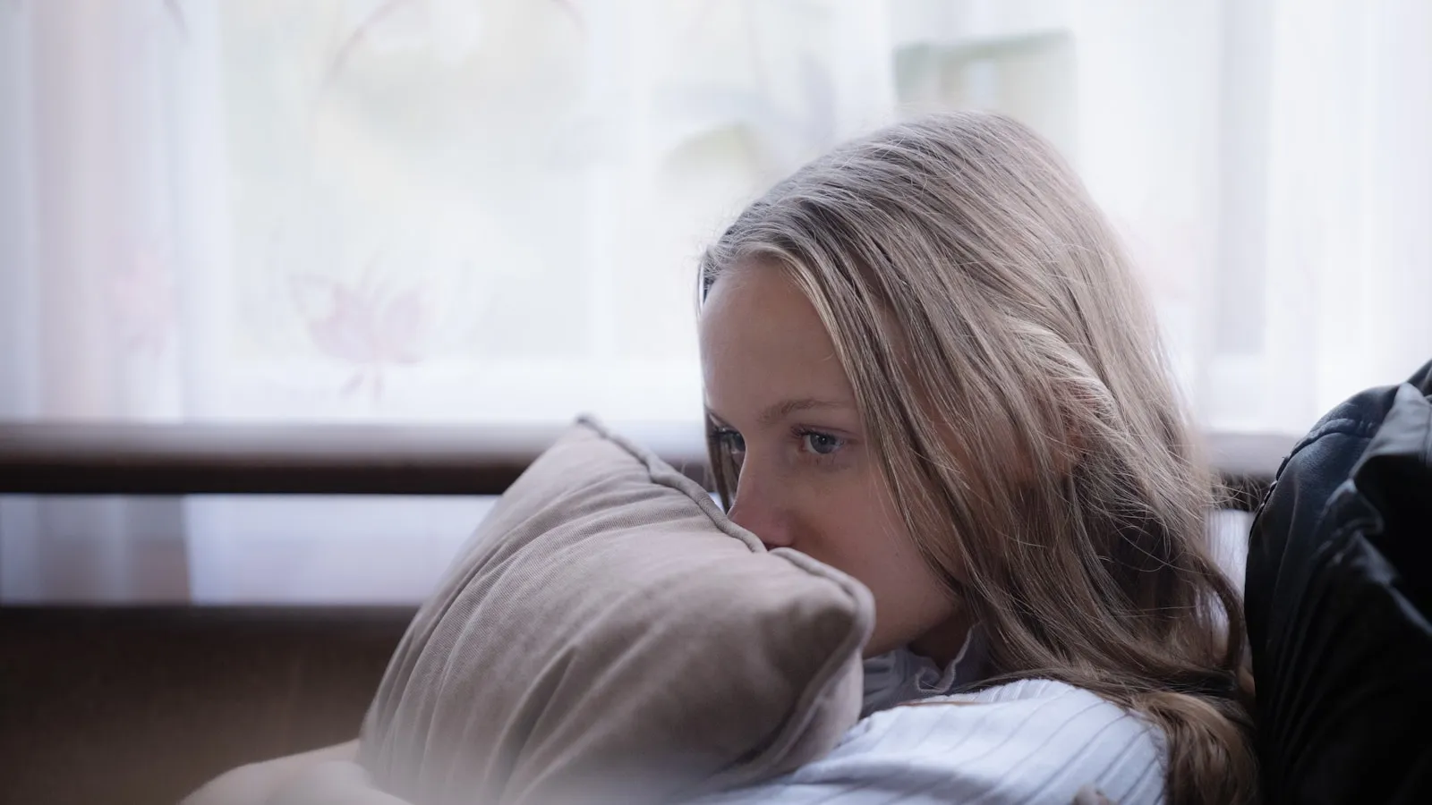 Vrouw zit rustig op een bank in een lichte kamer.