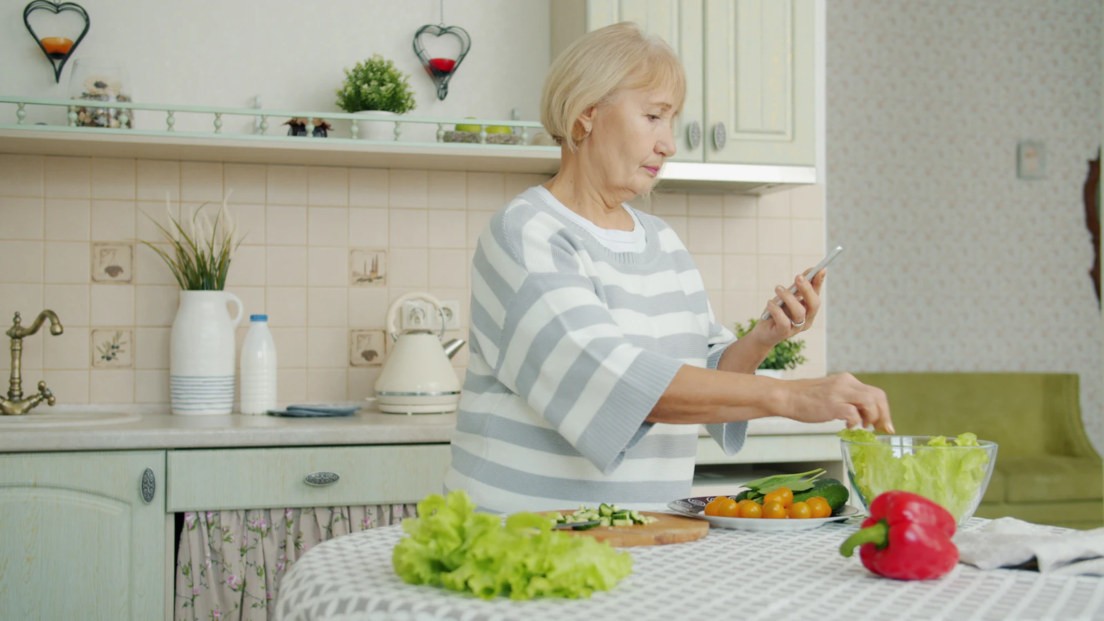 Vrouw maakt een salade klaar in haar keuken en kijkt op haar telefoon.