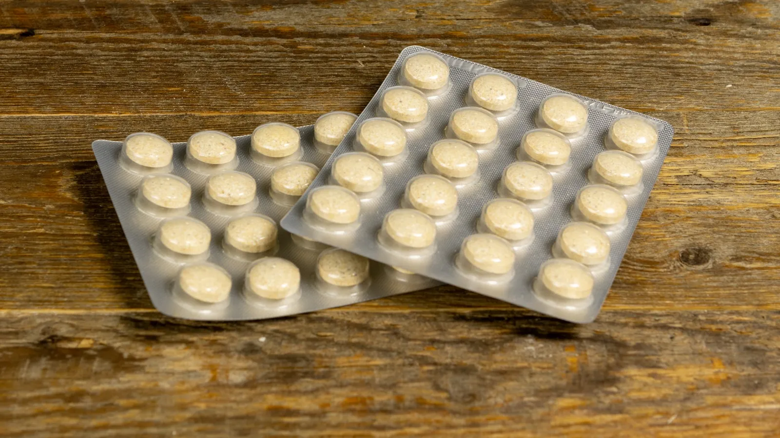 Twee doordrukstrips met lichte tabletten op een verweerd houten tafelblad.