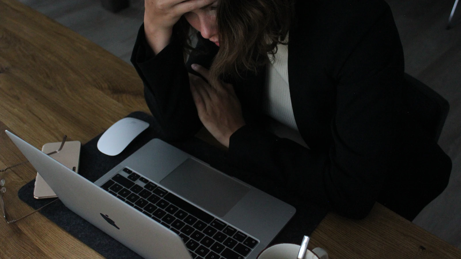Vrouw zit met haar hoofd in haar handen achter een laptop.