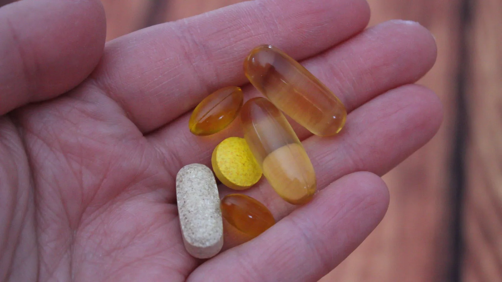 Open hand met zes supplementen: vier softgelcapsules en twee tabletten.
