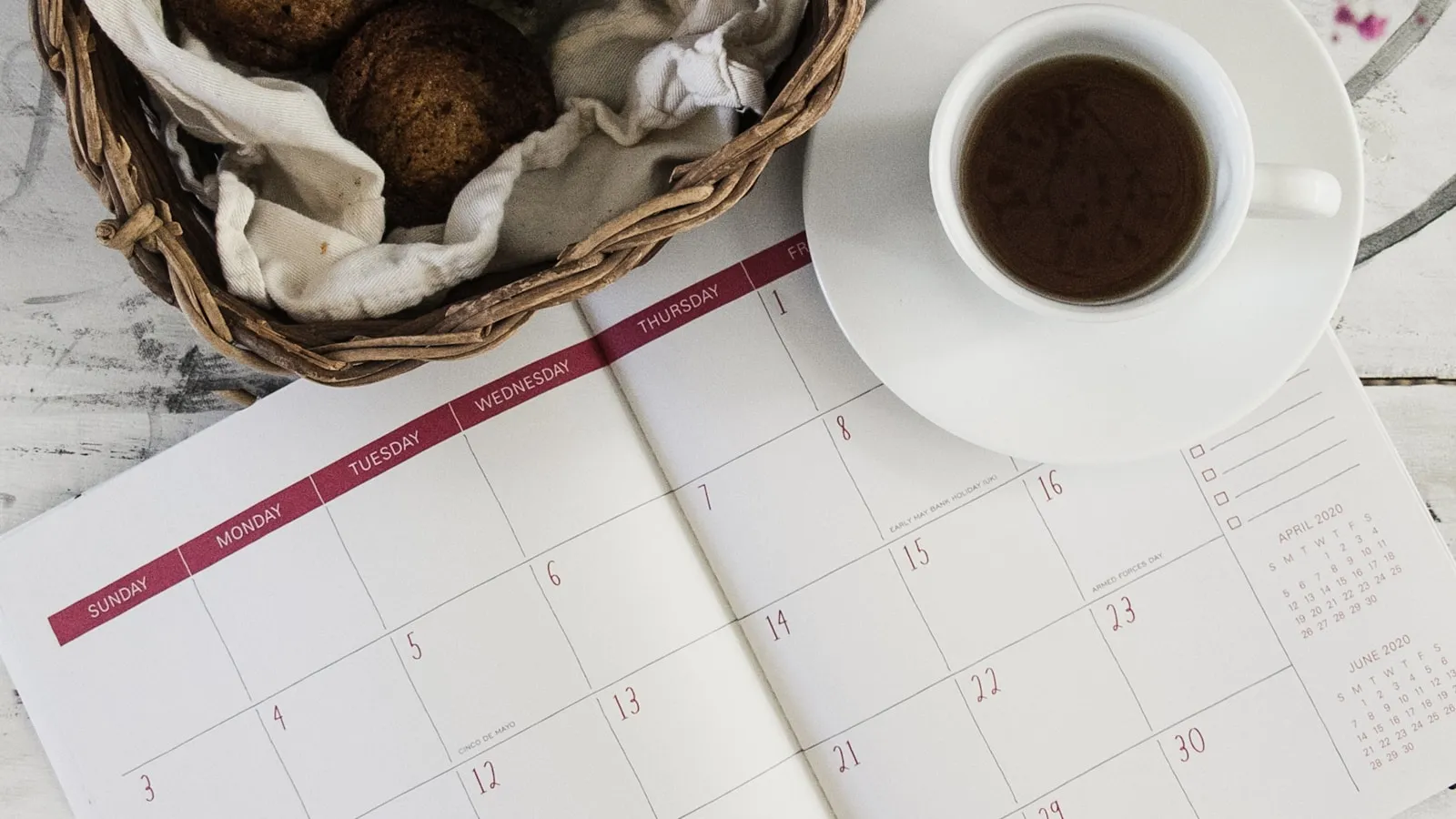 Opengeslagen maandkalender op een witte tafel, met een kop koffie ernaast.