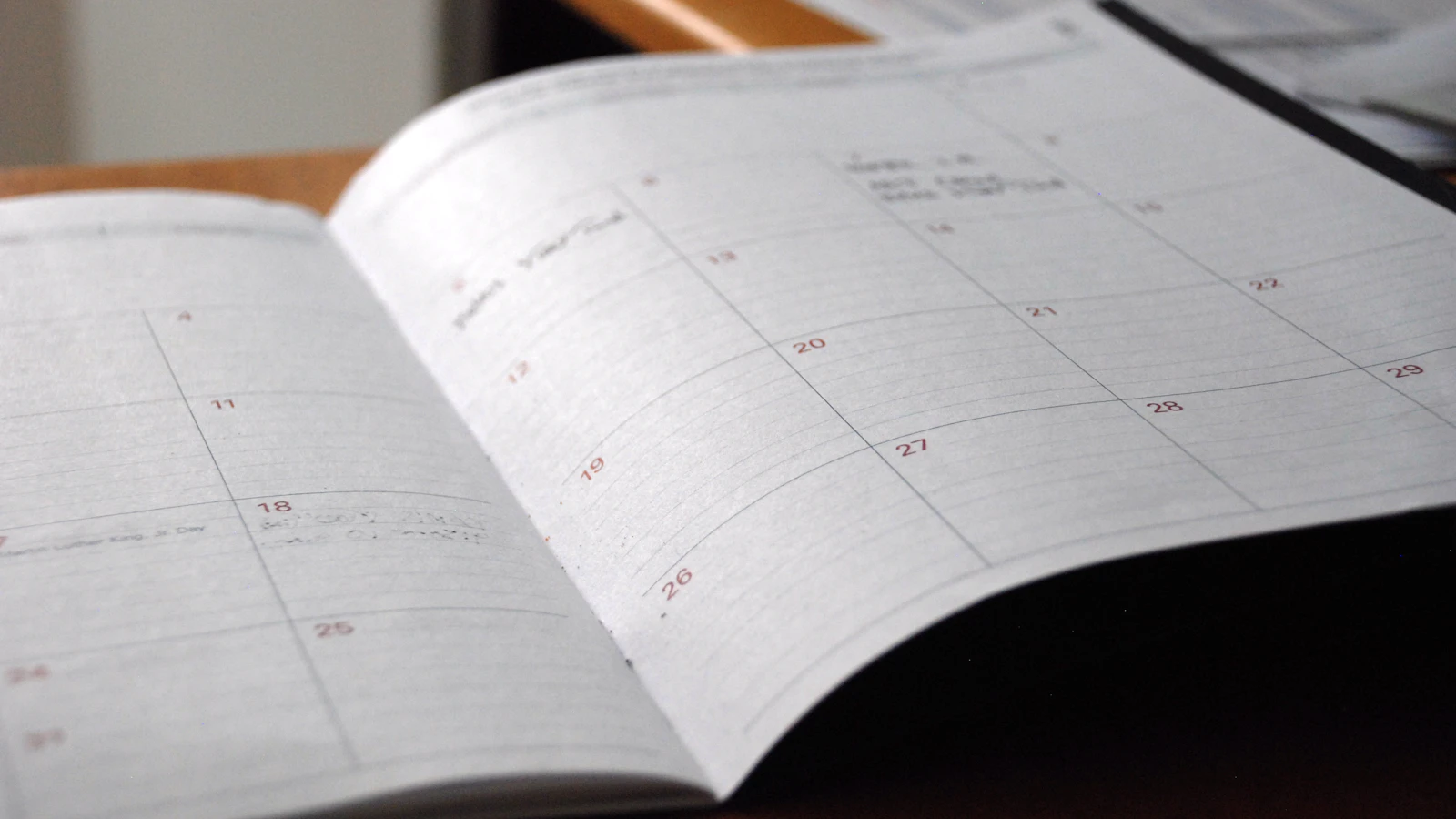 Een opengeslagen maandkalender op een houten bureau.