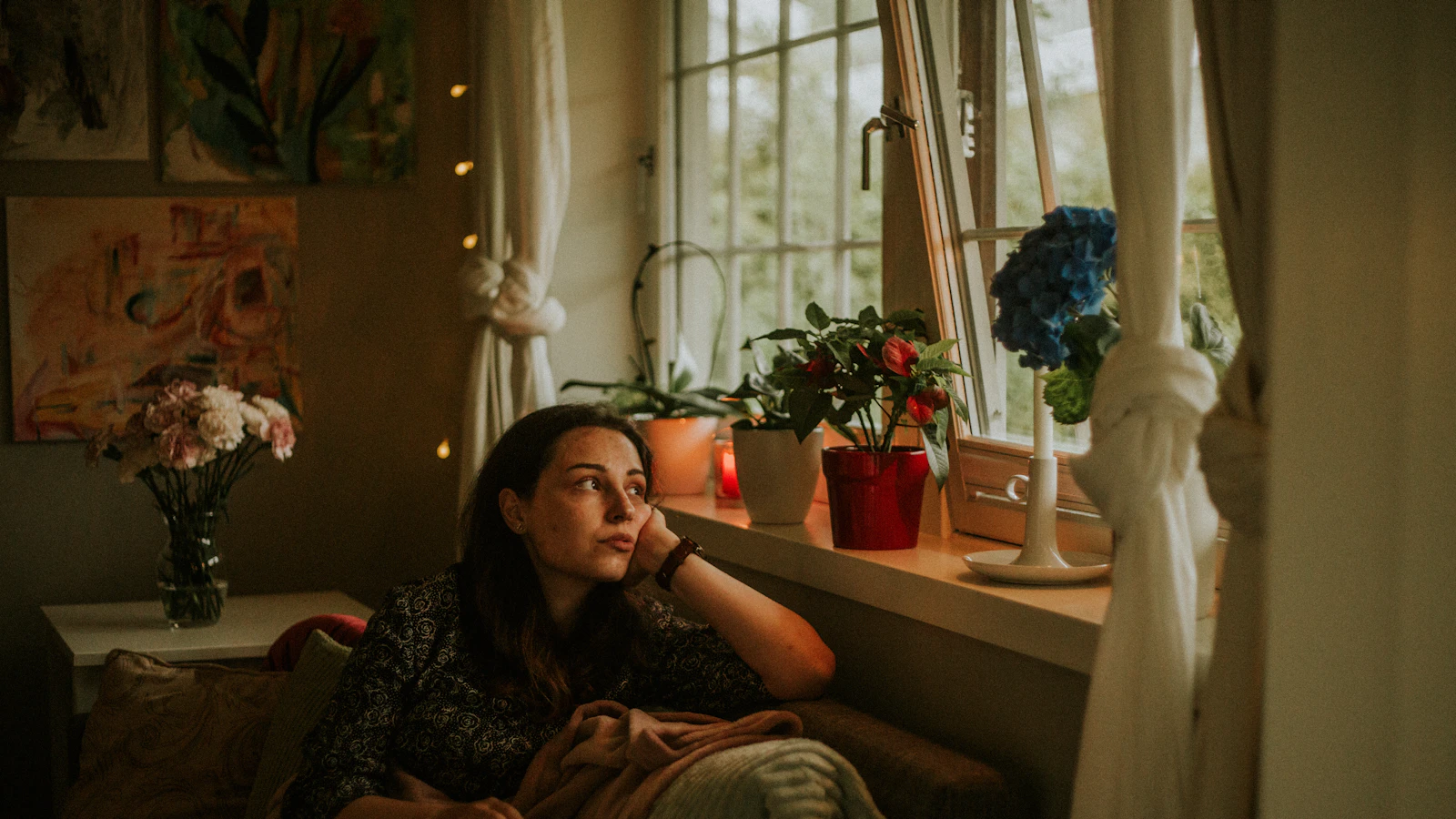 Vrouw kijkt nadenkend uit het raam in een rustige kamer.