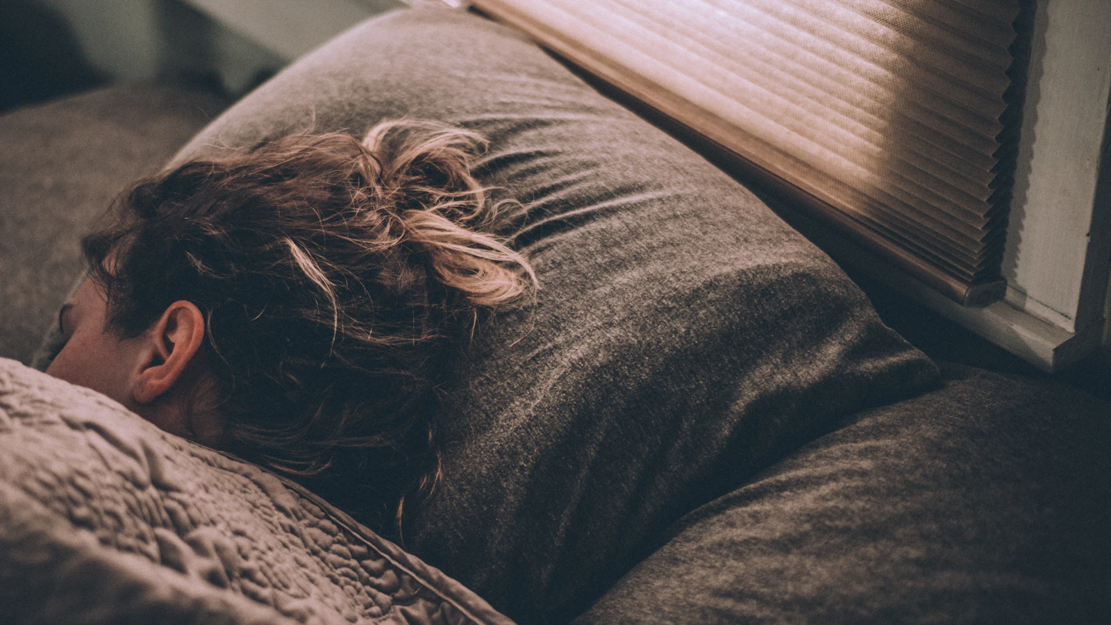 Vrouw ligt wakker in een koele, donkere slaapkamer.
