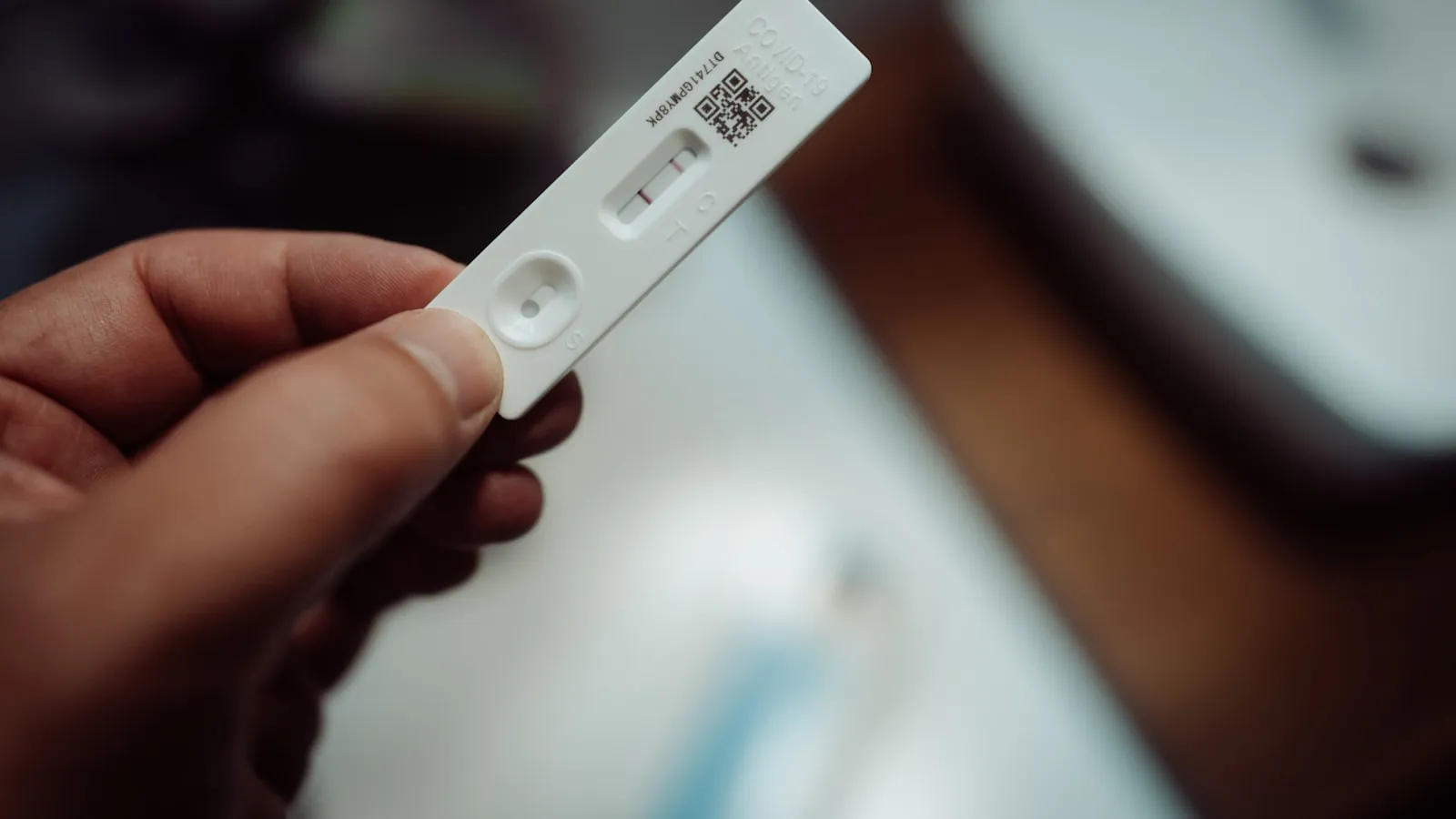 Vrouw houdt een zwangerschapstest van de drogist vast naast een buisje voor een hCG bloedtest