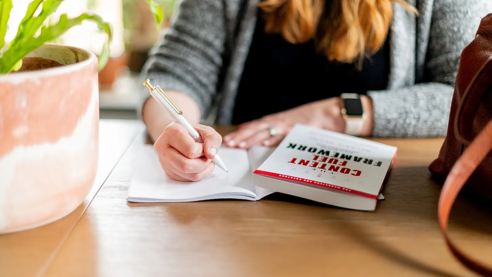 Een vrouw schrijft aantekeningen in een notitieboek aan een tafel.