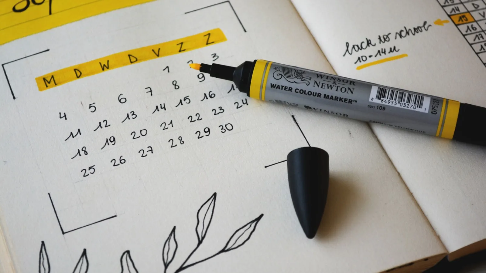 Handgetekende maandkalender in een notitieboek met een gele marker ernaast.