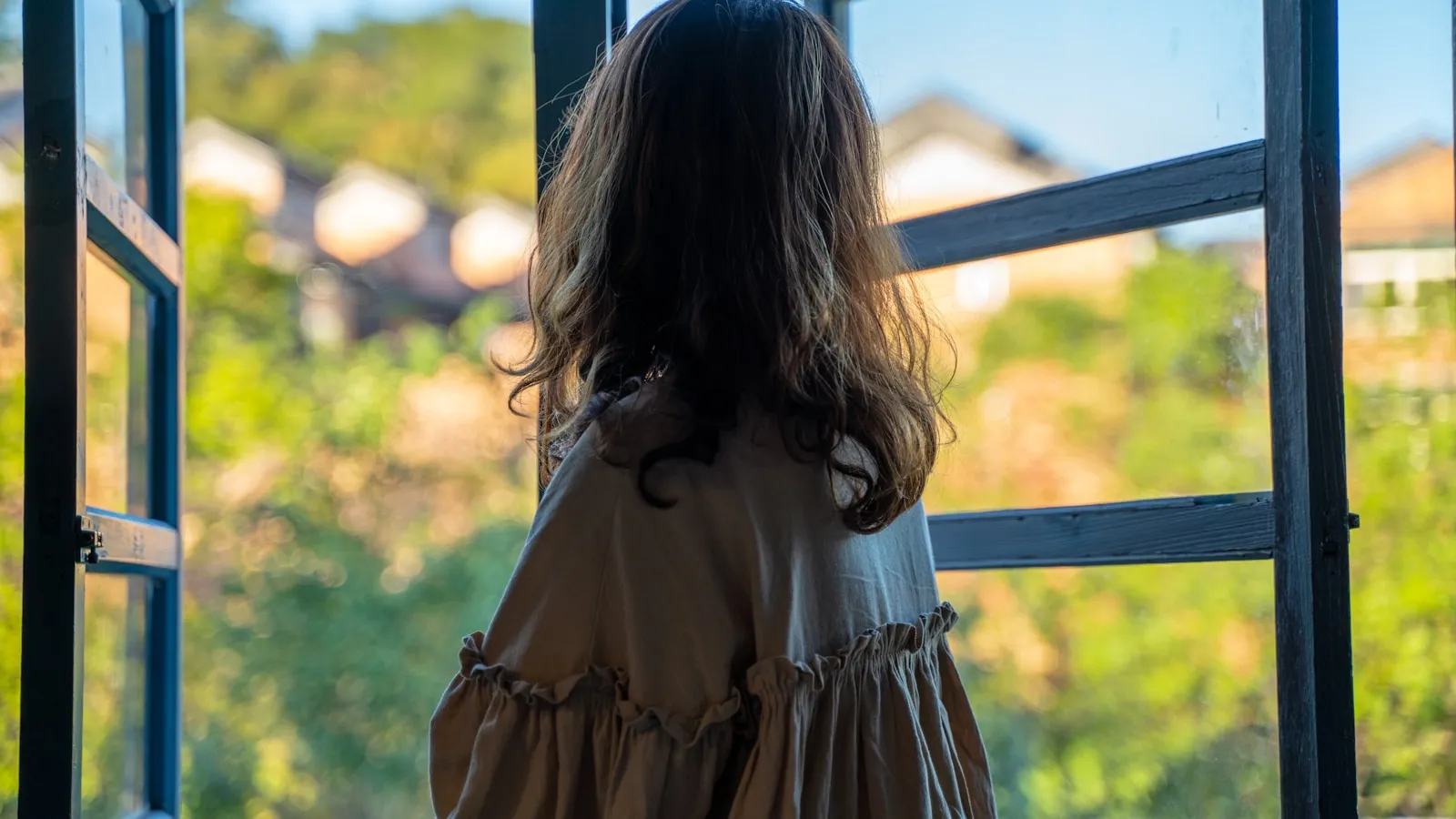 Vrouw zit rustig bij een raam met daglicht en kijkt kalm naar buiten.