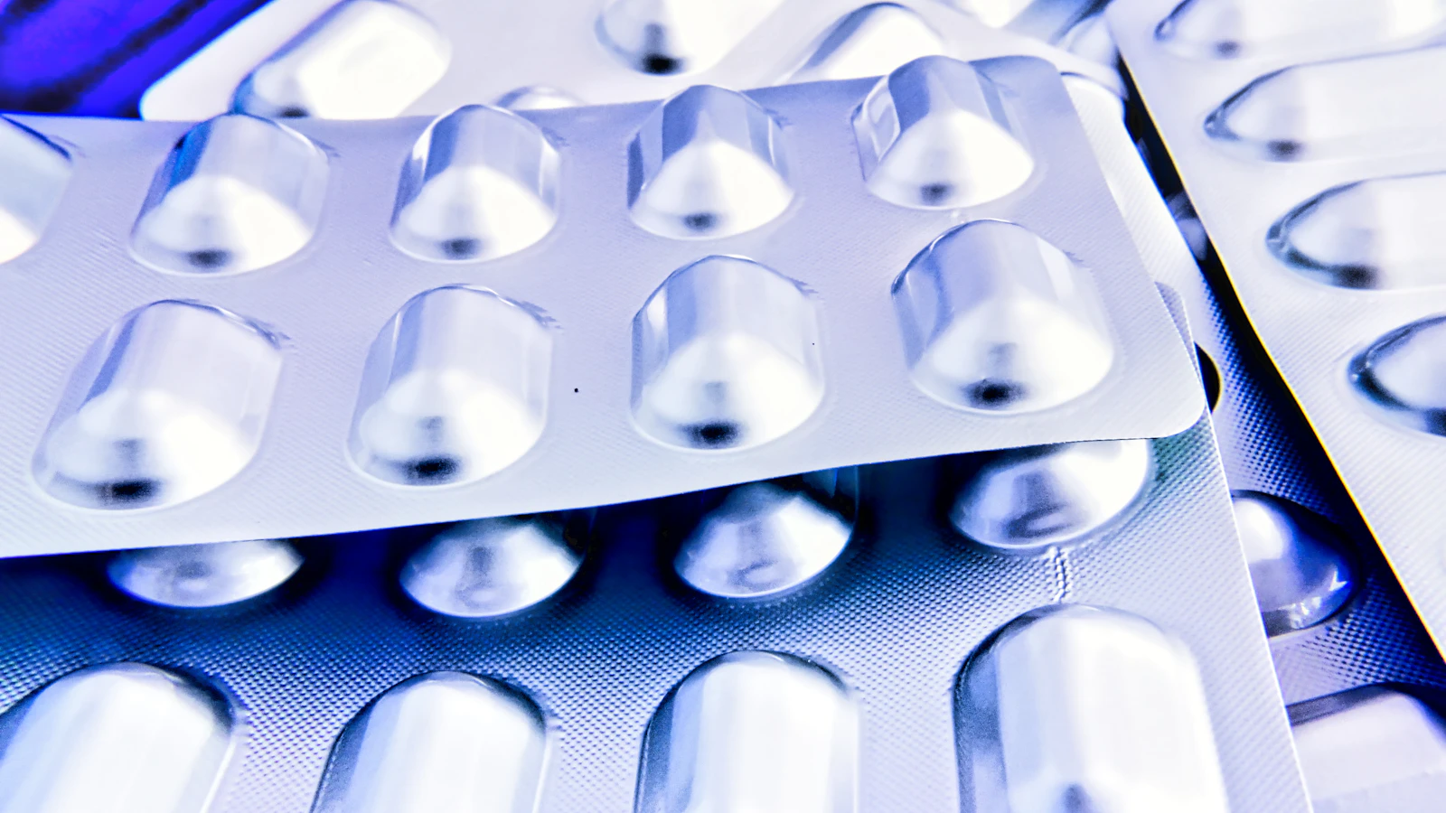 Close-up van zilverkleurige doordrukstrips met tabletten in blauwpaars licht.