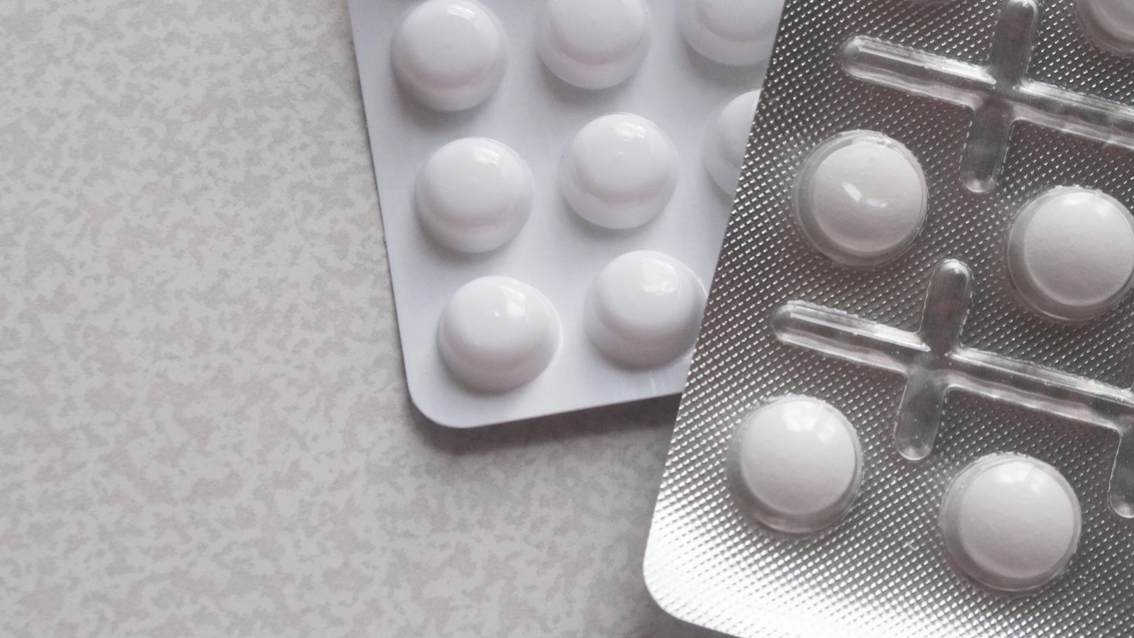 Twee doordrukstrips met witte tabletten op een warmgrijze ondergrond.