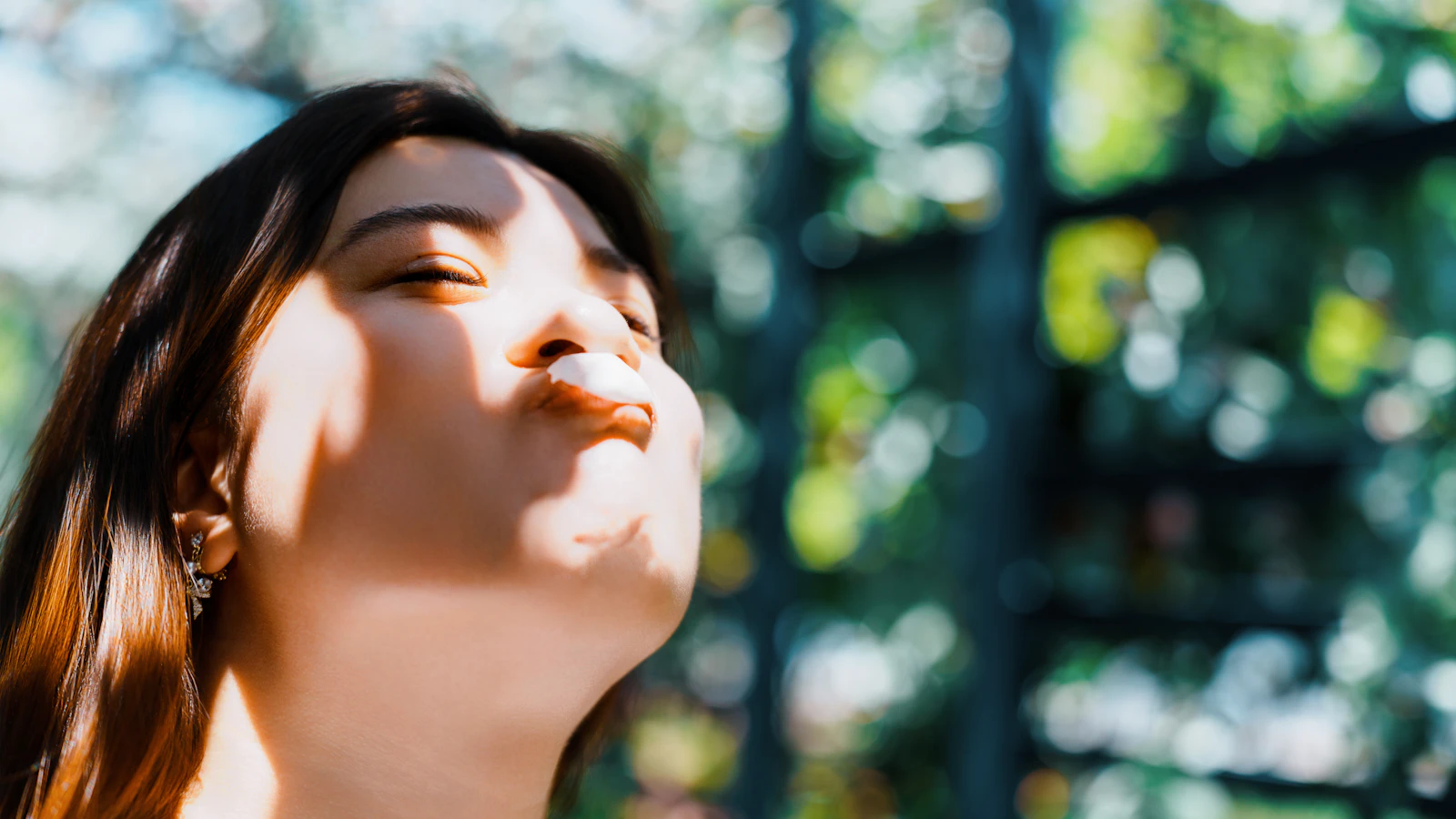Vrouw met gesloten ogen en de zon op haar gezicht buiten.