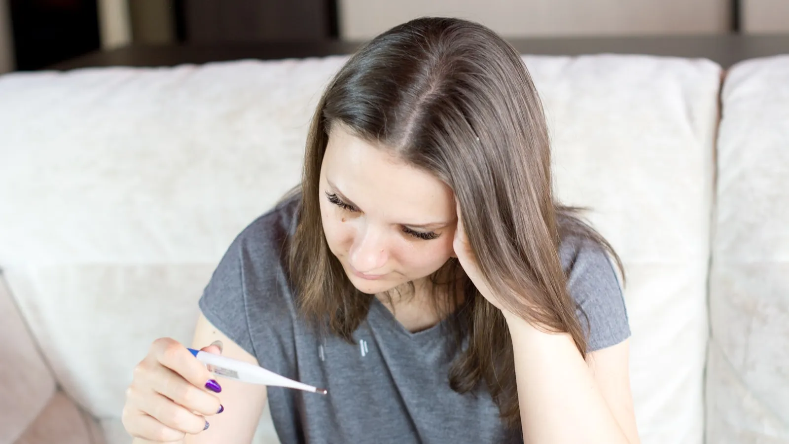 Vrouw zit op de bank en kijkt naar een zwangerschapstest in haar hand.